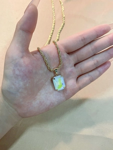Macro shot of rectangular multi-color stone pendant with gold rope chain on satin