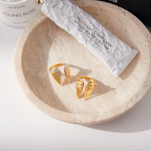 Detailed view of two-tone stainless steel wing rings on an elegant beige stone tray
