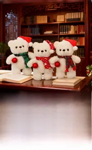 Tre orsetti di peluche con cappelli natalizi e sciarpe che tengono palline rosse