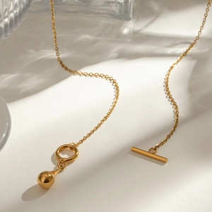 Detail of gold teardrop pendant necklace with OT toggle clasp on a ripple background
