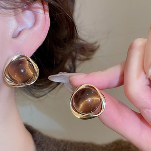 Detail of 18k gold-plated stud earrings with large round tiger eye stones on model