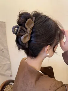 Dettaglio della pinza per capelli con fiocco in pelle marrone su una coda bassa