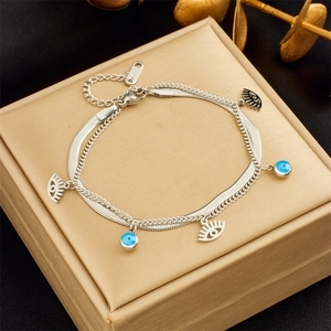 Silver double-layer bracelet with evil eye and eyelash pendants on a gold jewelry box