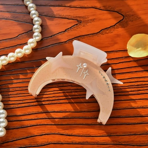 Detail shot of a crescent moon hair claw in nude pink with rhinestones and star patterns