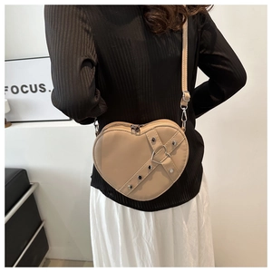 Model draagt een hartvormige beige crossbody tas met klinknagels en gesp