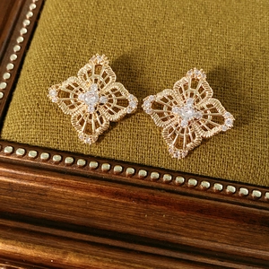 Macro detail of hollow rose gold flower earrings with pavé zircons on green velvet