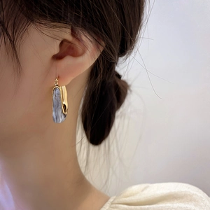 Detail view of U-shaped earrings featuring blue marbled texture and gold metal frame