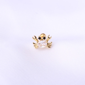 Détail macro d'un piercing d'oreille en forme de crabe doré orné de zircons brillants
