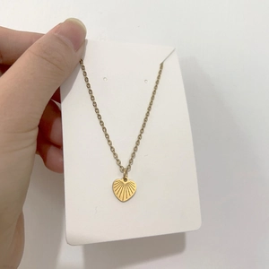 Detail of gold heart pendant with radial engravings on a fine link chain necklace