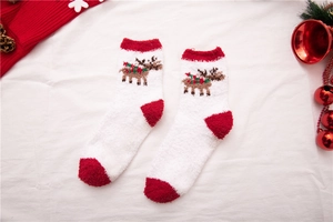 Detail von roten Weihnachts-Korallenfleece-Socken mit weißem Rentier-Muster und Festdeko