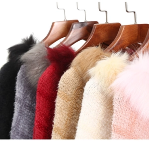Close-up of fluffy faux fur collars on diverse knitted capes hanging on wooden hangers