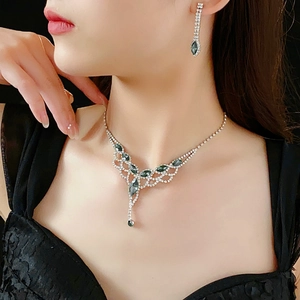 Close-up of elegant silver necklace and tassel earrings set with green gems and rhinestones