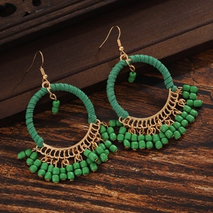 Detail of green handmade bohemian bead earrings with gold fan charm on wood background
