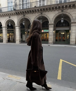 Lungo trench marrone scuro con cintura abbinato a una borsa a mano in pelle coordinata