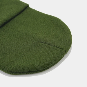 Détail macro du bonnet en tricot vert foncé montrant la texture côtelée et les coutures en laine