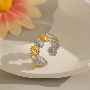 Two-tone gold and silver shell-shaped open ring displayed on a beige textured tray