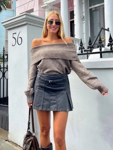 Pull en tricot marron à épaules dénudées avec une jupe plissée grise et ceinture