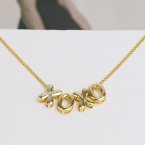 Macro shot of polished 18k gold plated brass XOXO pendant on a delicate link chain