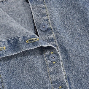 Detail eines hellblauen Jeanskleids mit gelben Ziernähten und blauen Kunststoffknöpfen