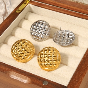 Macro view of gold and silver quilted pattern round button earrings on a beige cushion