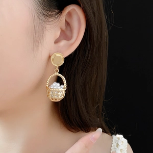 Close-up of vintage golden basket earrings with pearls worn by a model on black background