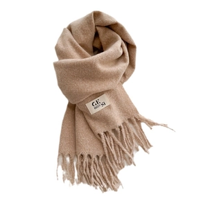 Beige soft knit scarf with fringe details and a minimalist brand label on white background