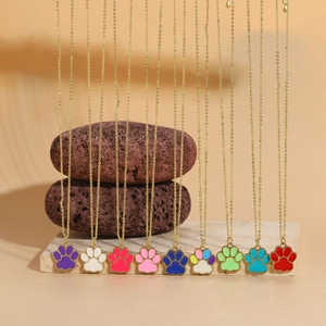 Macro shot of colorful paw print enamel pendants on gold chains over stone decor