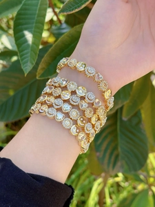 Detail of gold bracelets featuring smiley faces and sunflowers with zircon on the wrist