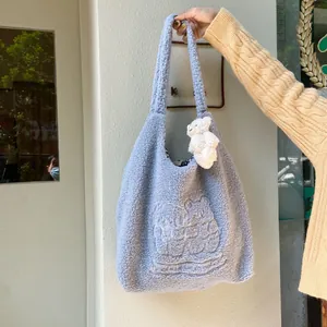 Close-up of light blue fleece tote bag with bear embroidery and plush charm pendant