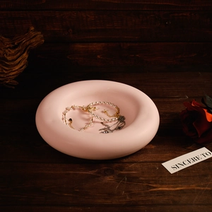 Pink matte torus jewelry tray holding pearl necklace on vintage wood background