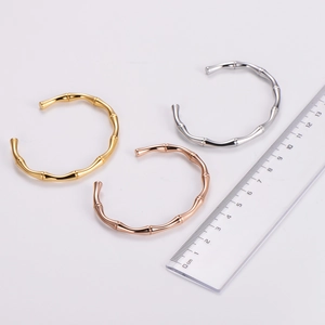 Trio of polished bamboo-shaped open bracelets in gold, silver, and rose gold with a ruler