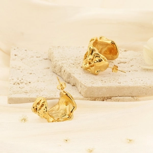 Minimalist gold irregular C-shape earrings with lava texture on beige stone background
