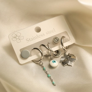 Detail of stainless steel earrings featuring evil eye and maple leaf charms in silver finish