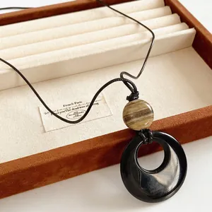 Collana lunga minimalista in agata con anello nero e perla marrone su base in legno