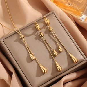 Golden teardrop earring and necklace set on beige silk background for elegant style