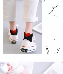 Close-up of white canvas sneaker paired with black ankle sock featuring a red heart heel tab