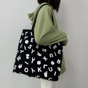 Black canvas tote bag with white graphic prints worn by a model against a white wall