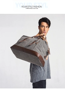 Man carrying a large grey canvas travel duffel bag with brown leather trim details