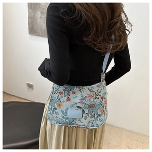 Detail of floral embroidery and leather logo on a light blue linen crossbody tote bag
