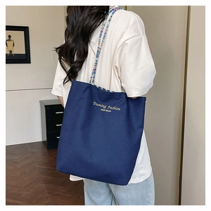 Detalle del bolso tote de lona azul marino con correas tejidas y bordado de la marca