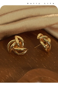 Macro shot of gold-plated twisted stud earrings on wood surface with silk background