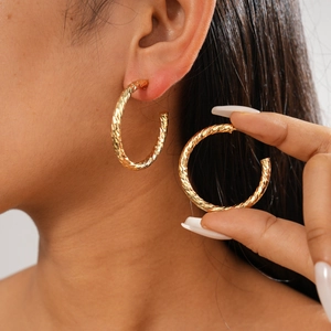 Close-up of golden geometric C-shaped earrings with diamond-cut texture on model