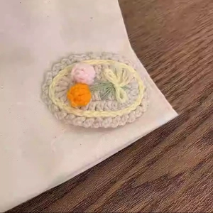Detail of handmade crocheted beige clip with pink and orange flowers and green bow