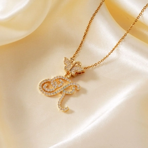 Golden butterfly and letter pendant necklace with sparkling cubic zirconia on silk background