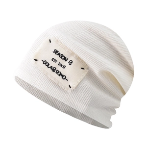 Detailed close-up of cream knit beanie with vintage fabric patch and ribbed texture