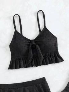 Detail van zwarte eyelet lace bikinitop met strik en ruches op een marmeren ondergrond