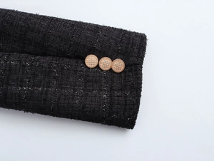 Vue détaillée de la manche du manteau en tweed noir avec trois boutons dorés texturés