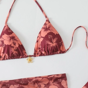 Close-up of tropical hibiscus print bikini with a decorative gold flower pendant detail