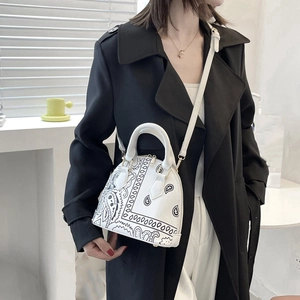 Detail of white shell bag with black paisley print and elegant gold zipper accent