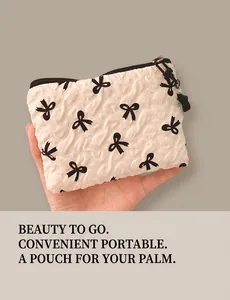 Quilted white cosmetic bag with black bow pattern and pearl zipper charm held in hand
